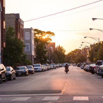 A person rides a motorcycle into the sunset on a neighborhood street in Chicago. Chicago has many popular neighborhoods close enough to downtown for a quick commute.